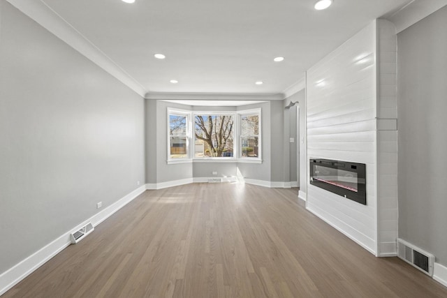 unfurnished living room with baseboards, visible vents, a glass covered fireplace, ornamental molding, and wood finished floors