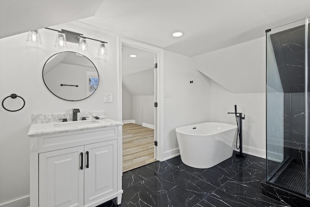 bathroom featuring marble finish floor, lofted ceiling, vanity, a freestanding tub, and baseboards