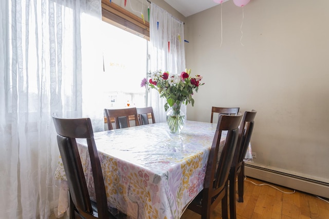 dining room featuring a baseboard heating unit, wood finished floors, and a healthy amount of sunlight