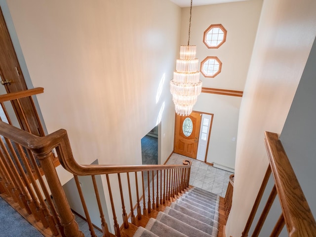 staircase with a baseboard heating unit, a high ceiling, baseboards, tile patterned floors, and an inviting chandelier