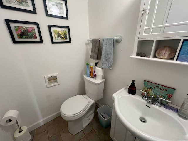 half bath featuring baseboards, a sink, toilet, and tile patterned floors