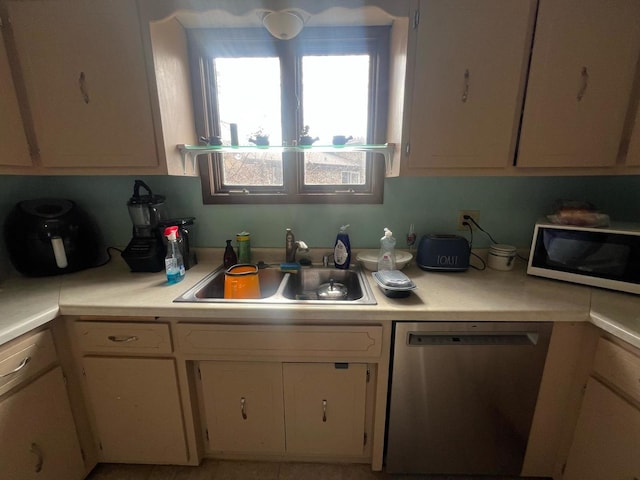 kitchen featuring light countertops, stainless steel dishwasher, a sink, and white cabinets