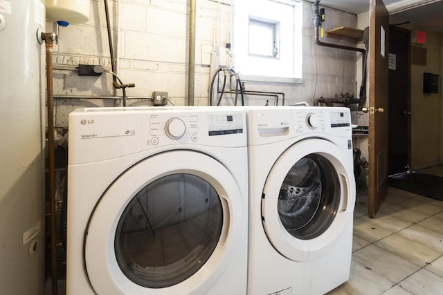 laundry area featuring water heater, concrete block wall, light tile patterned floors, laundry area, and washing machine and clothes dryer