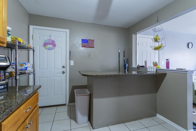 kitchen featuring dark stone counters, light tile patterned flooring, brown cabinetry, and baseboards