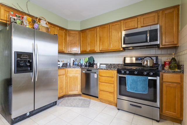 kitchen with dark stone counters, brown cabinetry, backsplash, and stainless steel appliances