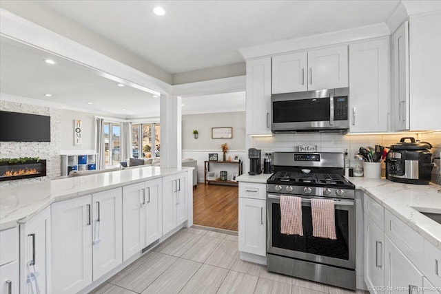 kitchen with light stone counters, a fireplace, decorative backsplash, appliances with stainless steel finishes, and white cabinetry