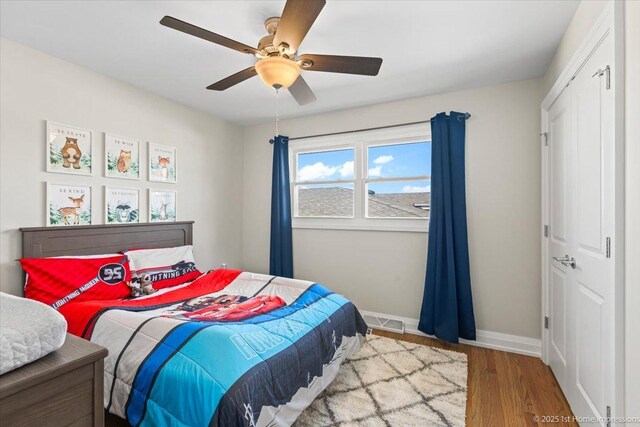 bedroom with a ceiling fan, wood finished floors, visible vents, baseboards, and a closet