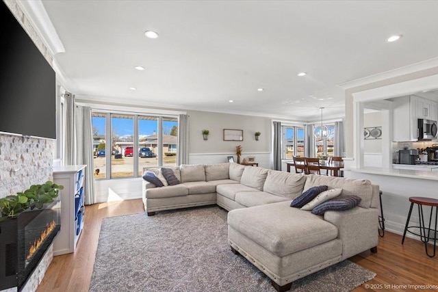 living room featuring light wood-type flooring, a lit fireplace, and ornamental molding