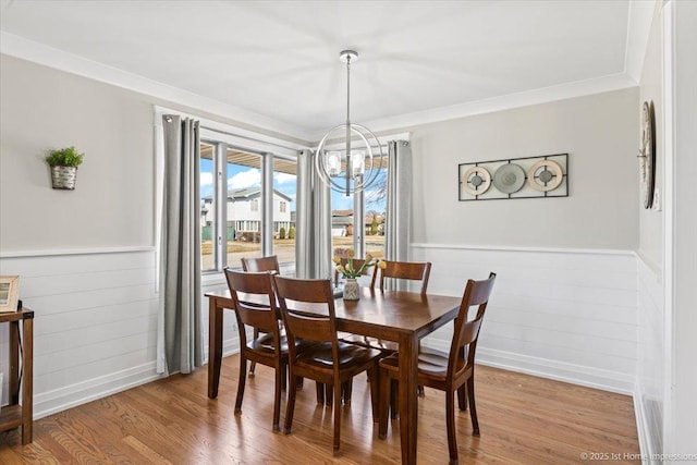 dining room featuring ornamental molding, light wood-style floors, a wainscoted wall, and a chandelier