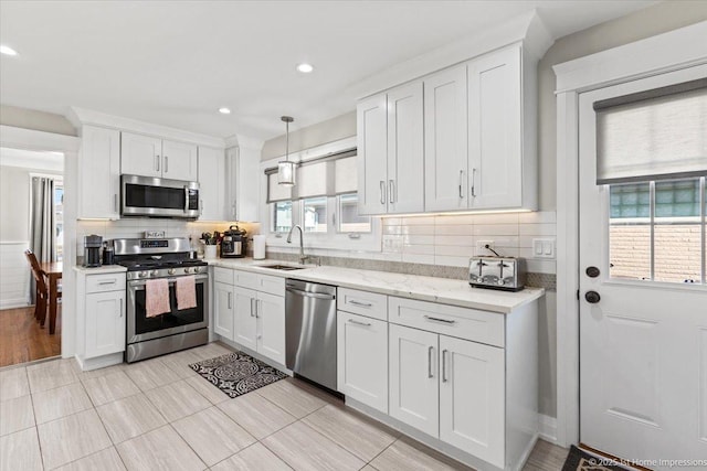 kitchen featuring decorative backsplash, hanging light fixtures, white cabinets, stainless steel appliances, and a sink