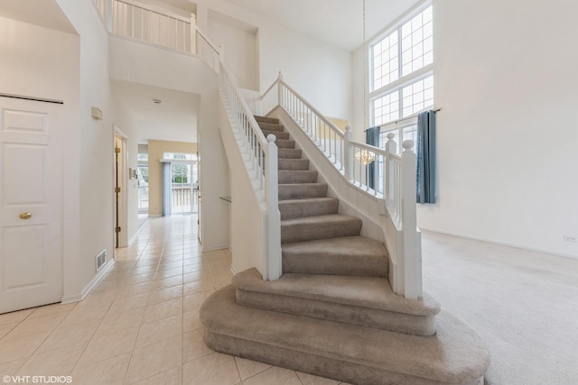 stairs featuring tile patterned flooring, visible vents, baseboards, carpet flooring, and a high ceiling