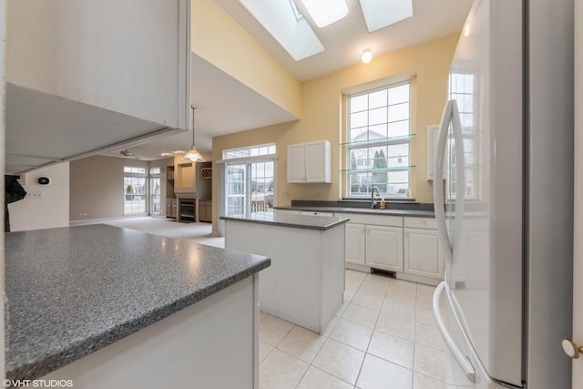 kitchen with a skylight, freestanding refrigerator, a sink, dark countertops, and a center island