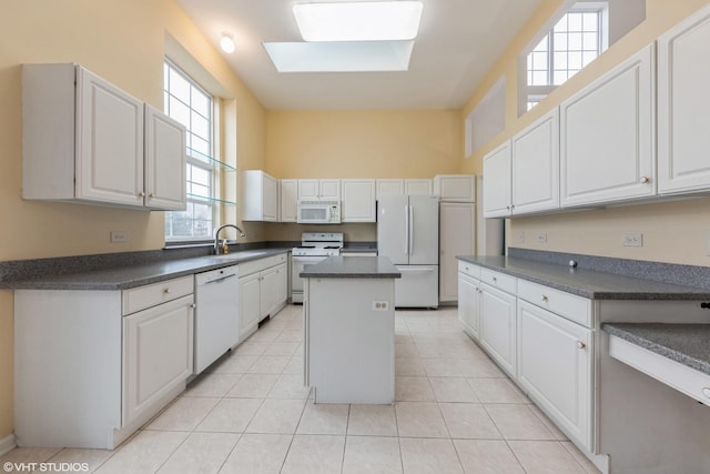 kitchen with white appliances, a skylight, dark countertops, and a sink