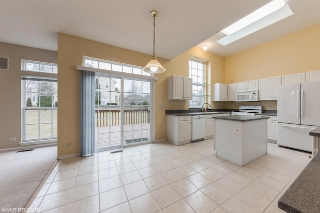 kitchen featuring dark countertops, a kitchen island, light carpet, a skylight, and white appliances