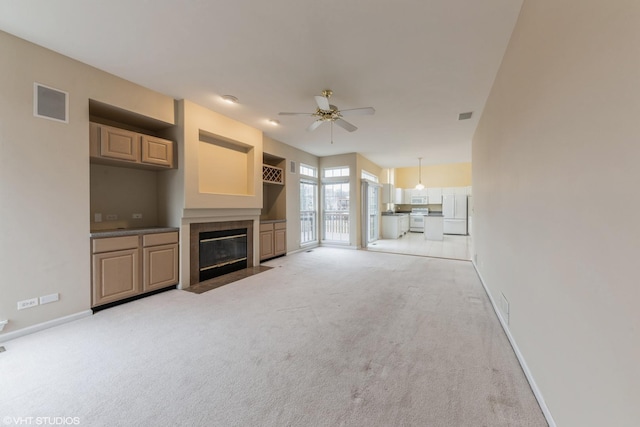 unfurnished living room featuring baseboards, light carpet, ceiling fan, and a fireplace