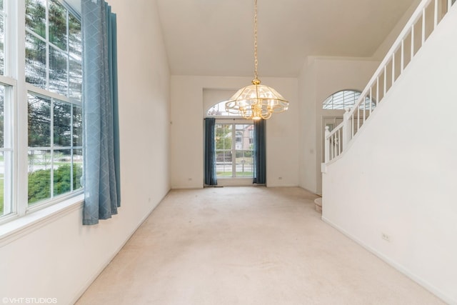 spare room with stairs, carpet, a chandelier, and a towering ceiling