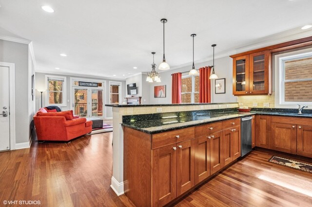 kitchen with brown cabinetry, a peninsula, dark stone counters, glass insert cabinets, and crown molding