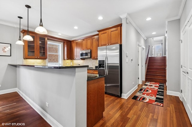 kitchen with brown cabinets, appliances with stainless steel finishes, a peninsula, glass insert cabinets, and dark wood-style flooring