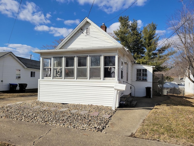 bungalow-style home with entry steps, a sunroom, fence, and a chimney