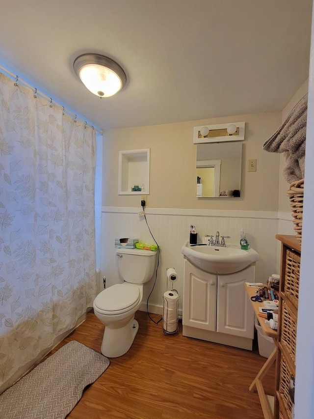 bathroom featuring toilet, vanity, wood finished floors, and wainscoting