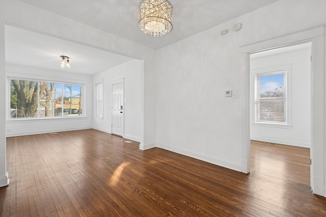 empty room featuring dark wood-style floors, baseboards, and a chandelier