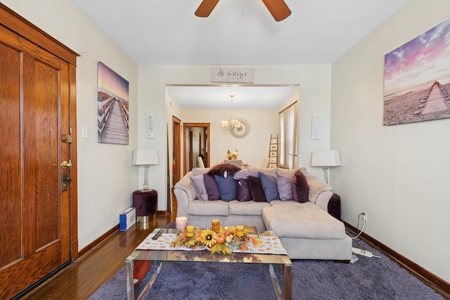 living area featuring baseboards, dark wood finished floors, and ceiling fan with notable chandelier