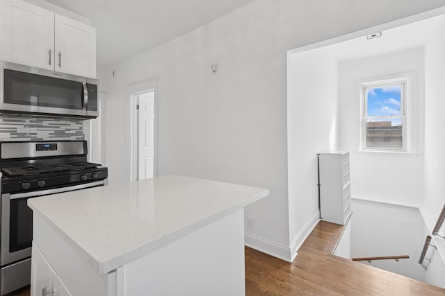 kitchen with a center island, baseboards, appliances with stainless steel finishes, wood finished floors, and white cabinetry