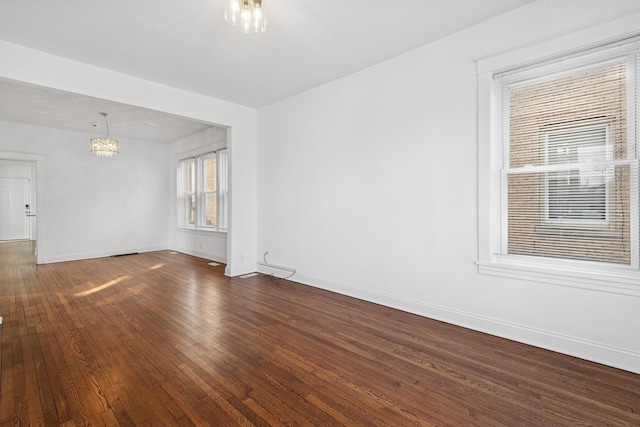 spare room featuring a chandelier, dark wood-type flooring, and baseboards