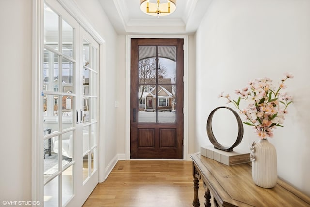 doorway featuring a tray ceiling, baseboards, crown molding, and light wood finished floors