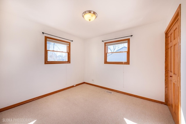 spare room with light colored carpet, visible vents, a wealth of natural light, and baseboards