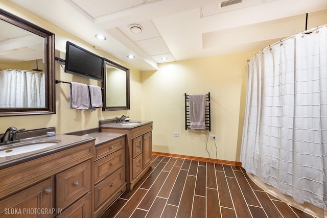 bathroom featuring baseboards, wood finish floors, double vanity, recessed lighting, and a sink