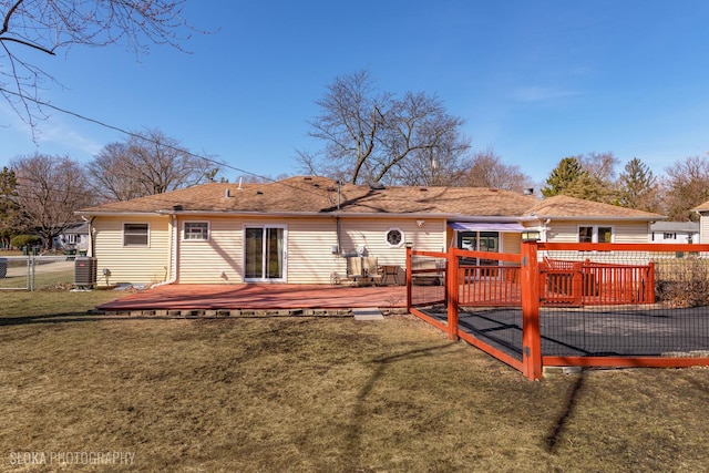 back of property with a lawn, a deck, central AC, fence, and a shingled roof