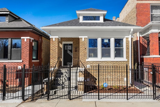 bungalow-style home featuring brick siding, a fenced front yard, and a shingled roof