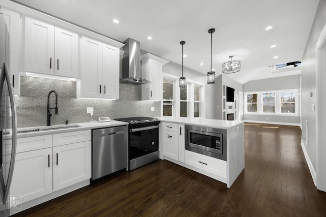 kitchen with a peninsula, a sink, light countertops, wall chimney range hood, and appliances with stainless steel finishes