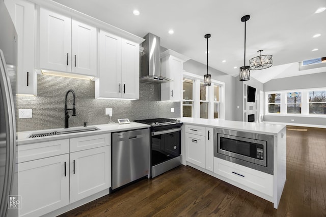 kitchen with light countertops, appliances with stainless steel finishes, a sink, wall chimney range hood, and a peninsula