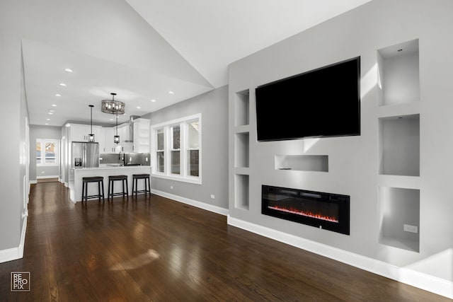 living area featuring built in shelves, dark wood finished floors, a wealth of natural light, and a glass covered fireplace