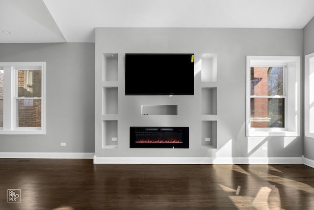 unfurnished living room featuring baseboards, built in features, wood finished floors, and a glass covered fireplace