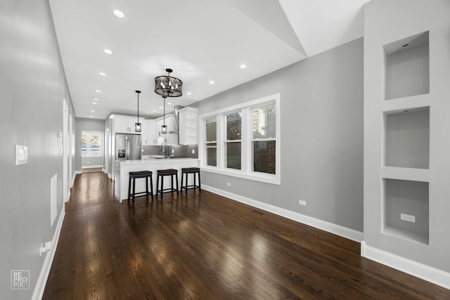 kitchen with dark wood-style flooring, white cabinetry, light countertops, stainless steel refrigerator with ice dispenser, and a kitchen bar