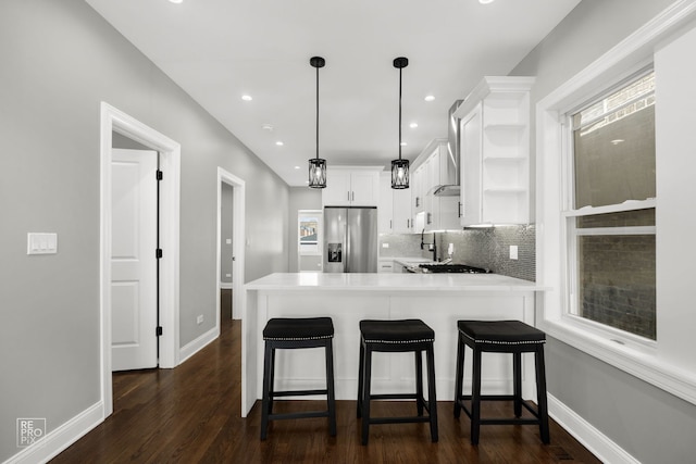 kitchen featuring dark wood-style flooring, light countertops, white cabinets, stainless steel fridge, and a peninsula