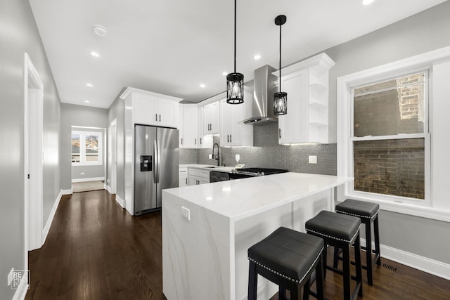 kitchen featuring tasteful backsplash, white cabinetry, wall chimney range hood, stainless steel fridge, and a peninsula