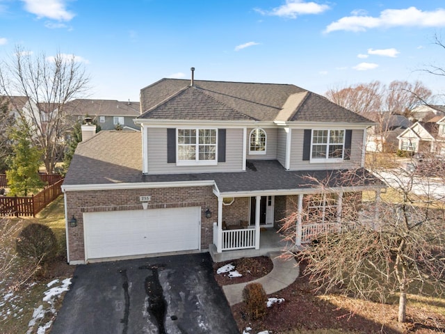 traditional-style home with aphalt driveway, roof with shingles, covered porch, fence, and brick siding