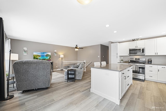 kitchen with light wood finished floors, a kitchen island, open floor plan, stainless steel appliances, and white cabinetry