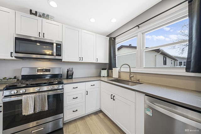 kitchen featuring recessed lighting, stainless steel appliances, a sink, white cabinets, and light wood-type flooring