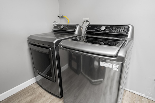 clothes washing area with laundry area, wood finished floors, washing machine and dryer, and baseboards