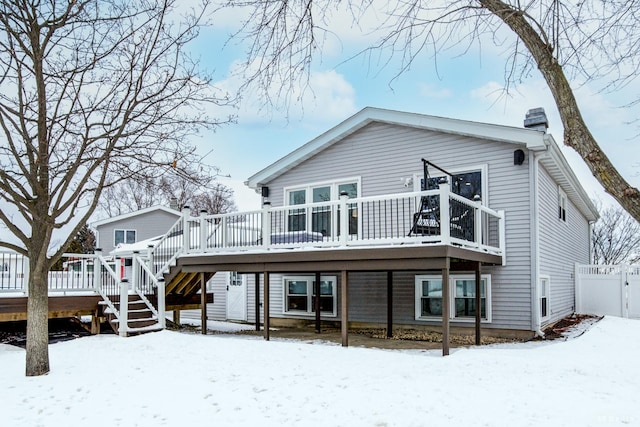 snow covered house featuring stairway, a chimney, a wooden deck, and fence