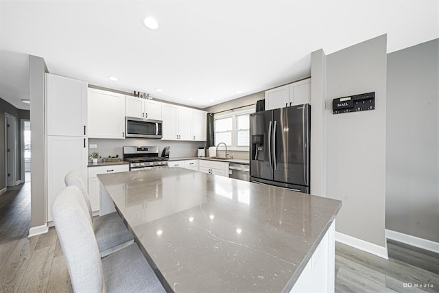 kitchen featuring white cabinets, a large island, light wood-style flooring, appliances with stainless steel finishes, and a sink