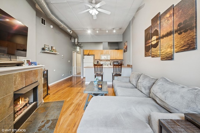 living area featuring a tiled fireplace, wood finished floors, a towering ceiling, rail lighting, and ceiling fan