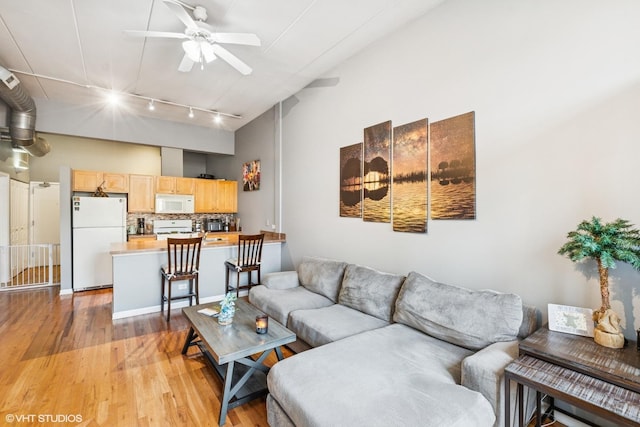 living room featuring light wood finished floors, rail lighting, ceiling fan, and a towering ceiling