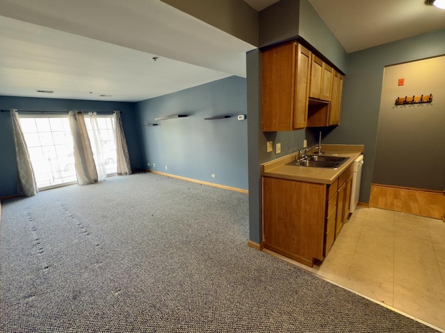 kitchen with light carpet, a sink, brown cabinetry, white dishwasher, and baseboards