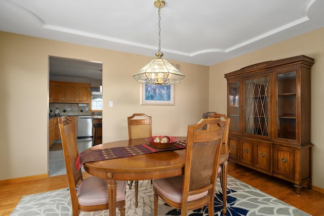 dining room featuring a raised ceiling, baseboards, and light wood finished floors